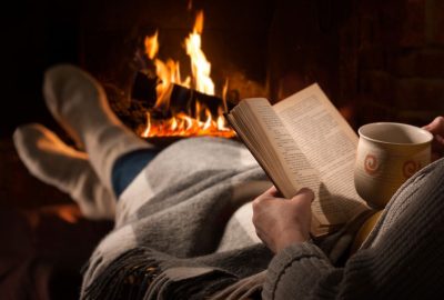 A woman reading a book by a fire. Winter fire safety tips.