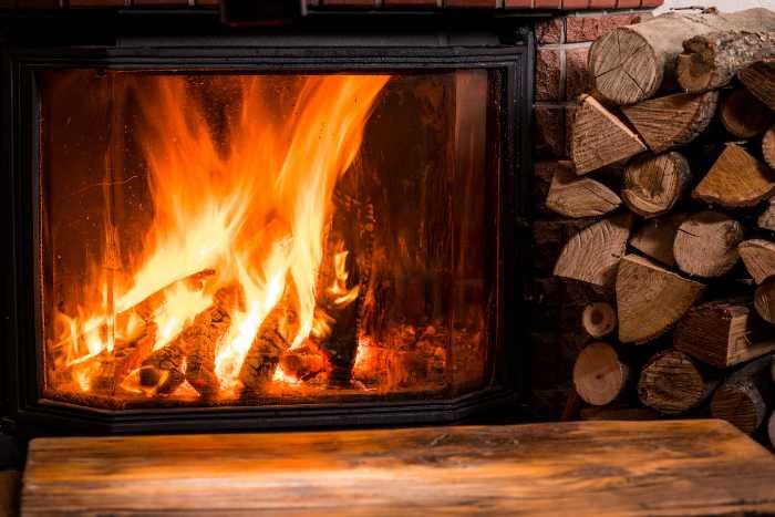 Image of a lit fireplace with a pile of chopped wood next to it