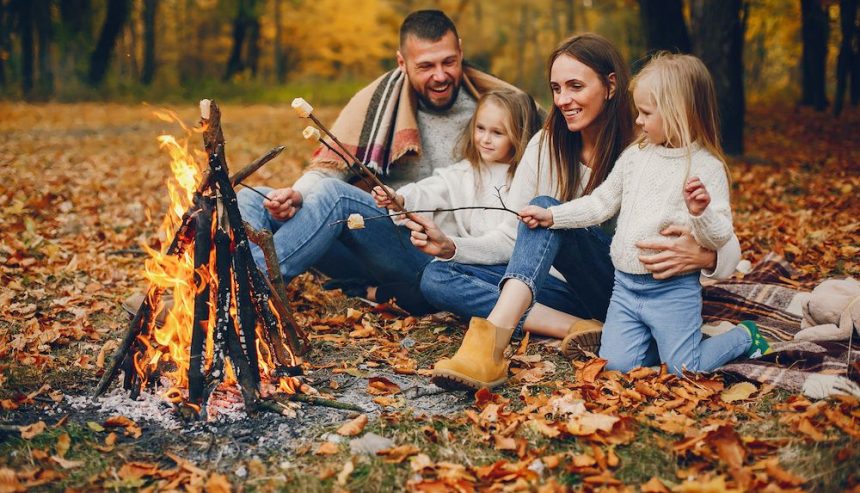 A family roasting marshmallows around a fire among fall foliage