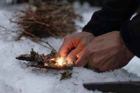 Male hands starting a fire in the snow. Winter fire safety tips.