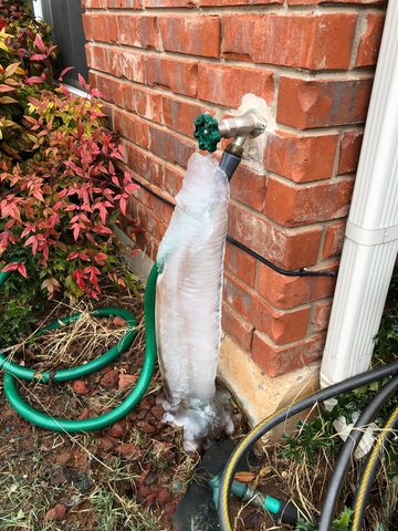 A frozen pipe and water spicket on the side of a house.