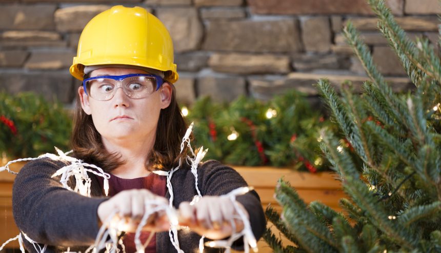 Woman plugging in Christmas lights with hard hat on after following holiday safety tips