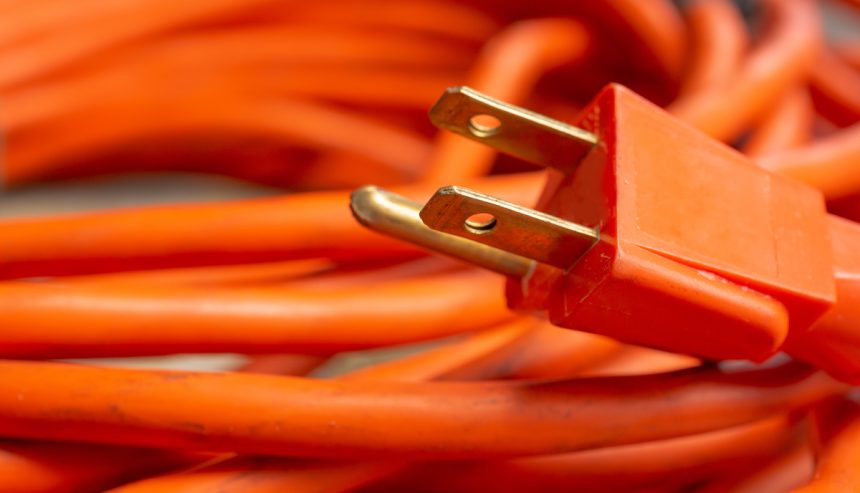 extention cord safety - a closeup view of a male end plug of a coiled orange extension cord.