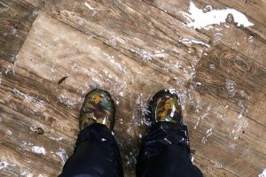 Picture of a set of boot-covered feet standing in water that is covering a hardwood floor