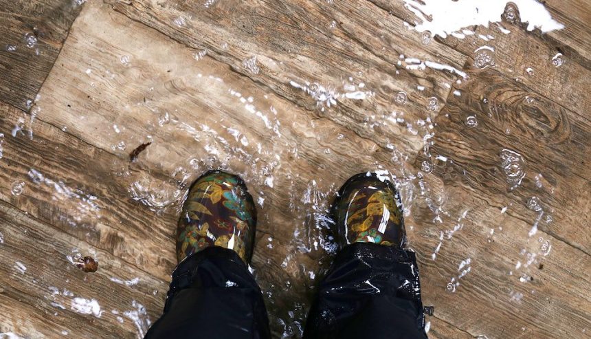 Picture of a set of boot-covered feet standing in water that is covering a hardwood floor