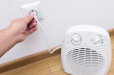 Person plugging in a small portable space heater into the wall.