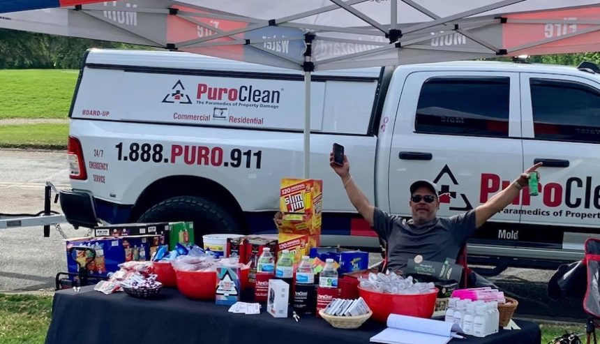 PuroClean booth set up with goodies and information. Man sitting at table to raise awareness.