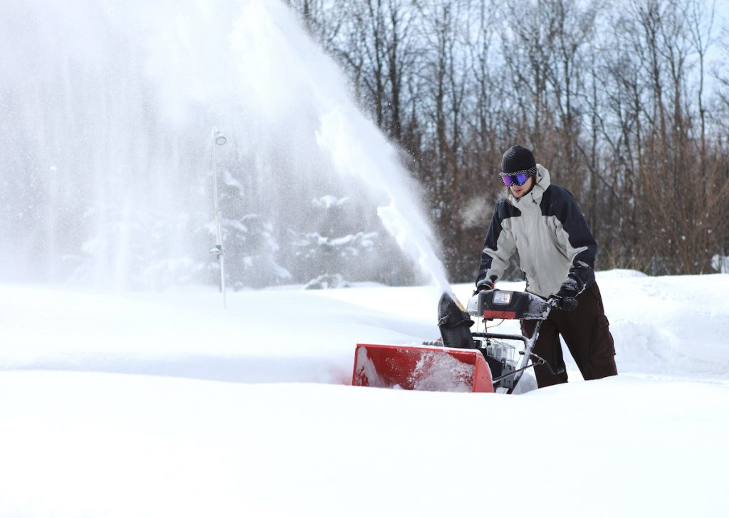 A man using a snow blower to remove snow.