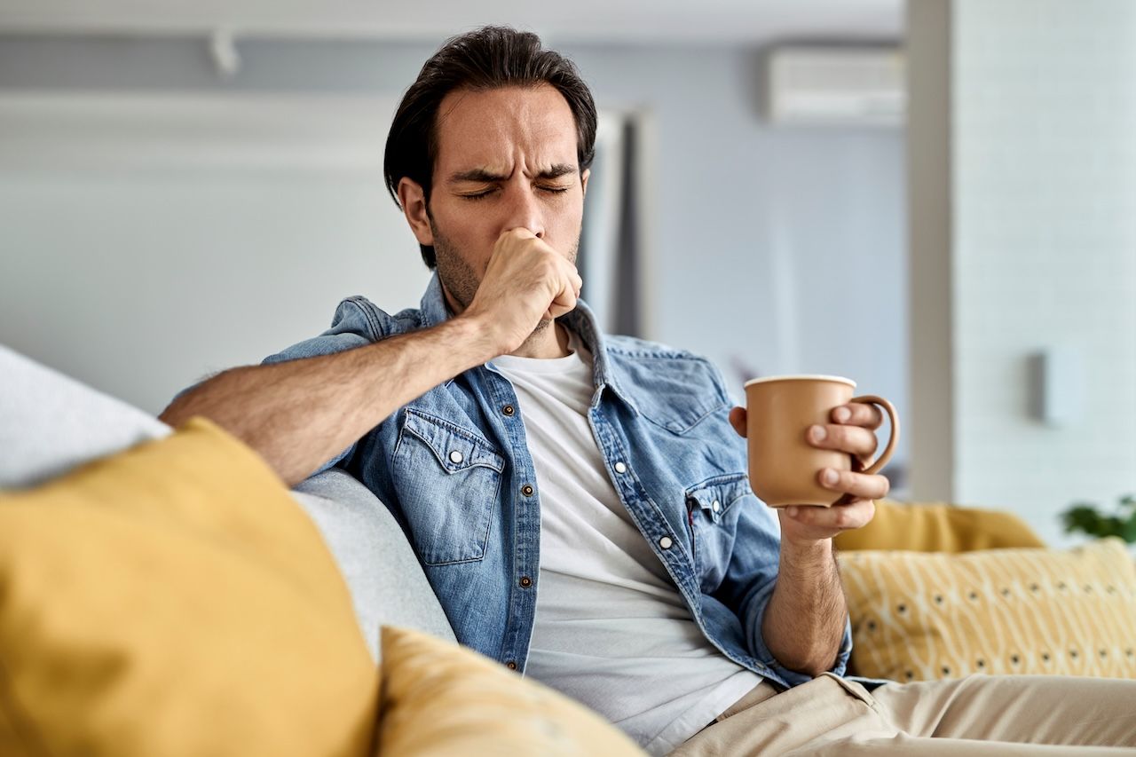 man coughing while holding a mug