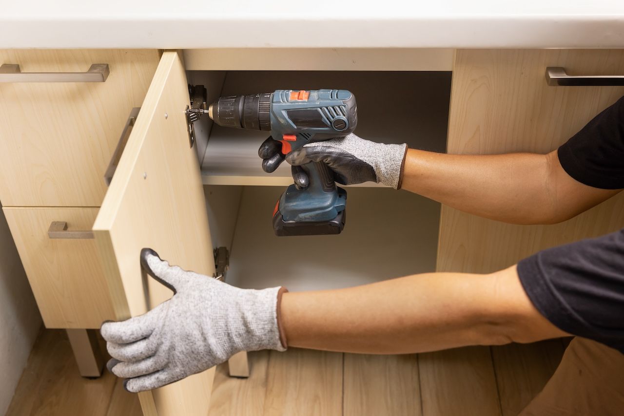 person with a drill fixing a cabinet door