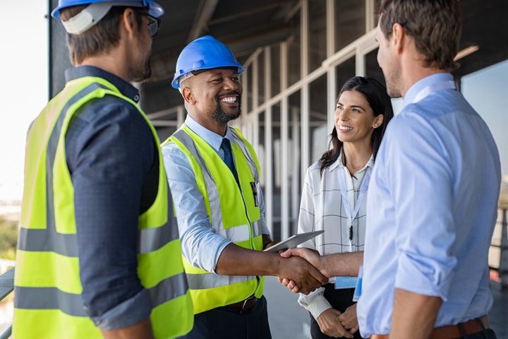 Man wearing hard hat shaking hands with a man, with two people looking on